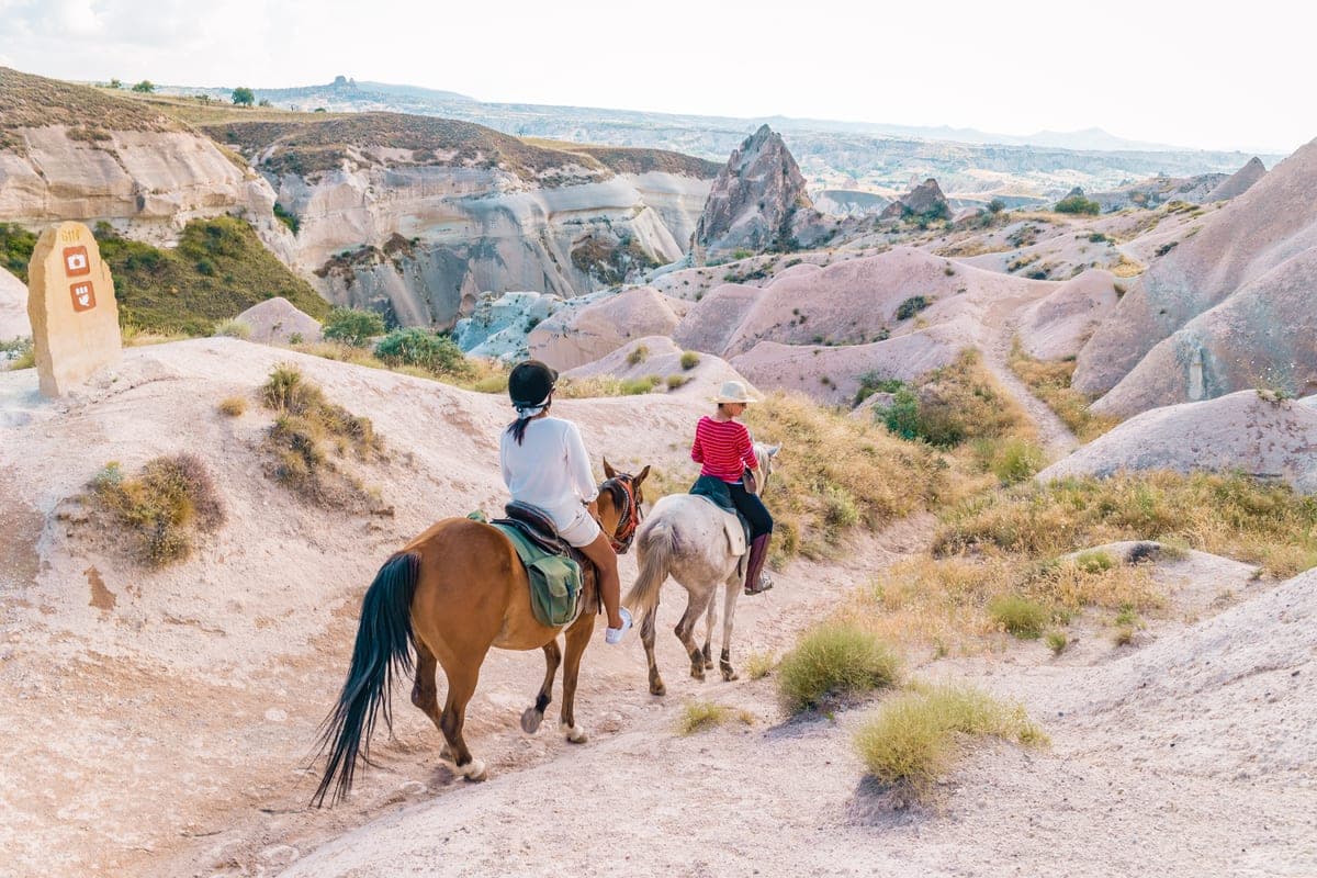 Two riders on a track above a pale tuff valley near Göreme